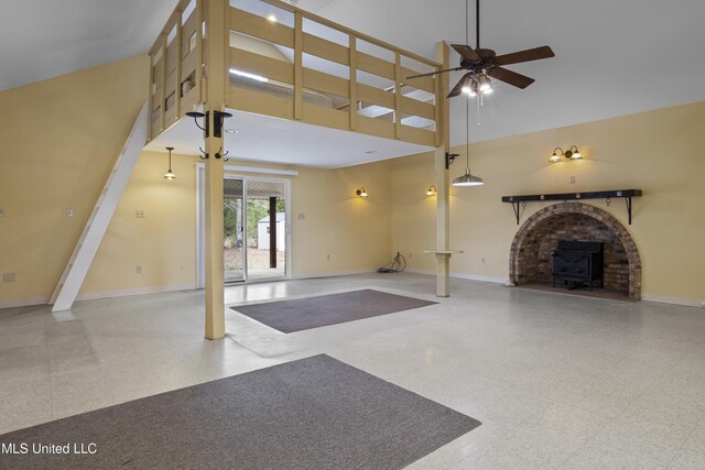 unfurnished living room featuring baseboards, a high ceiling, a wood stove, and a ceiling fan
