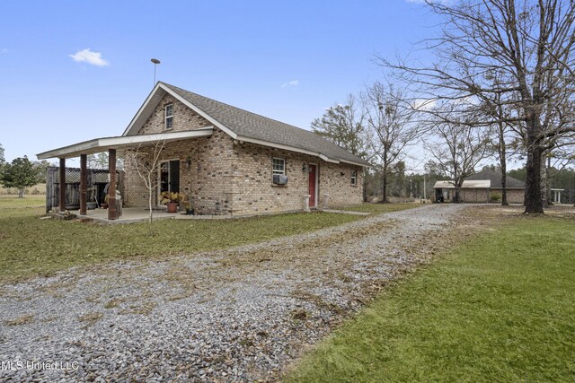 view of front facade featuring brick siding, a front lawn, a shingled roof, gravel driveway, and a patio