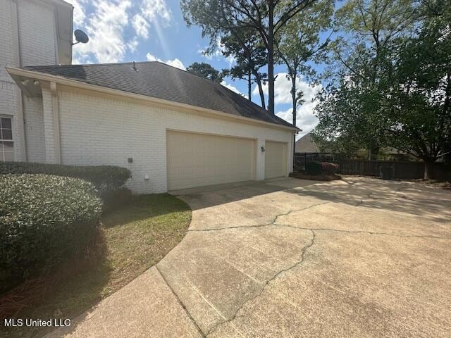 117 Peninsula Dr, Brandon, MS 39047 - view of side of home with fence, an attached garage, driveway, brick siding, and a shingled roof