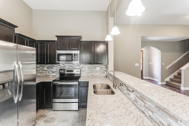 kitchen featuring appliances with stainless steel finishes, a sink, arched walkways, and light stone countertops