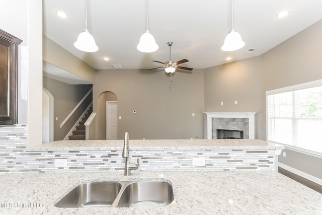 kitchen with a sink, a ceiling fan, decorative backsplash, a tile fireplace, and arched walkways