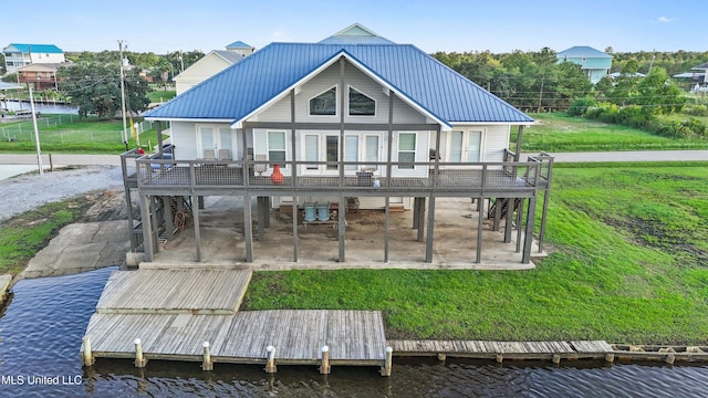 rear view of house with a deck with water view, a patio, a carport, and a lawn