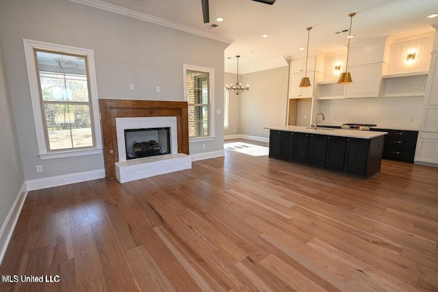 kitchen with backsplash, a brick fireplace, pendant lighting, a center island with sink, and light hardwood / wood-style flooring