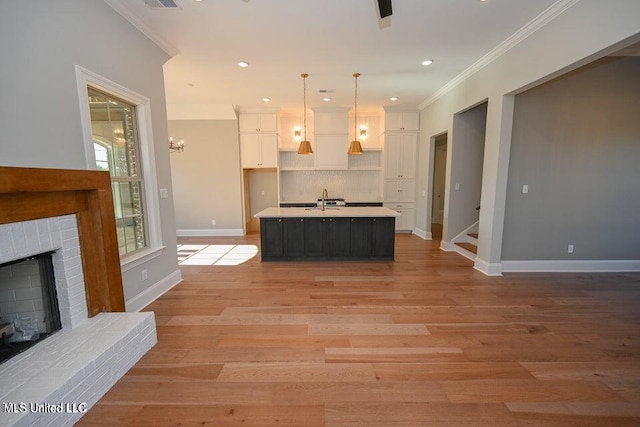 kitchen featuring a brick fireplace, crown molding, pendant lighting, a center island with sink, and white cabinetry