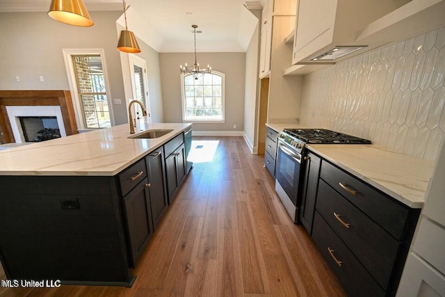 kitchen featuring stainless steel gas stove, decorative light fixtures, a center island with sink, and sink