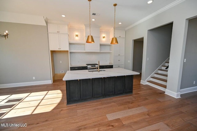 kitchen with pendant lighting, a kitchen island with sink, white cabinets, sink, and ornamental molding