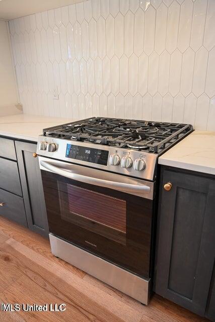 kitchen featuring light wood-type flooring, tasteful backsplash, and stainless steel gas range oven