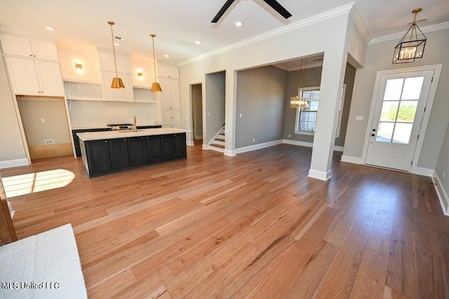 kitchen featuring backsplash, a center island with sink, ceiling fan with notable chandelier, hanging light fixtures, and white cabinetry