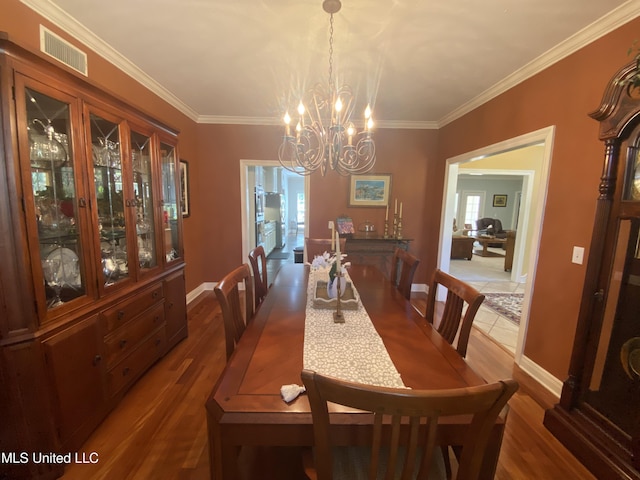 dining room with crown molding, wood finished floors, a notable chandelier, and visible vents