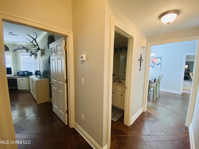 hall featuring dark tile patterned floors, baseboards, and a sink