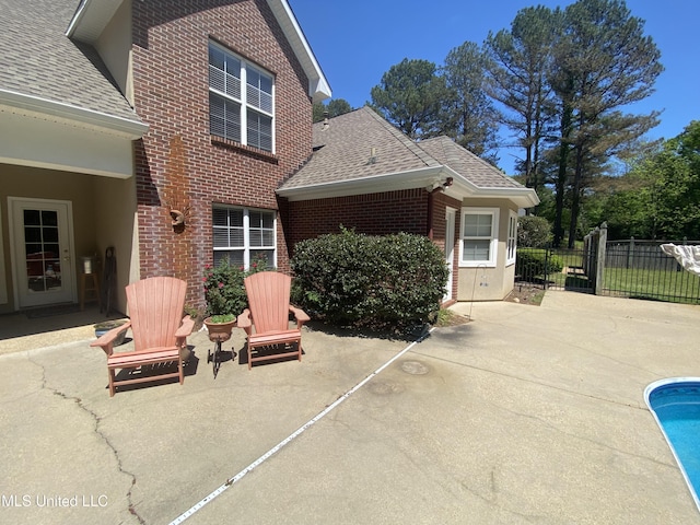 back of property featuring roof with shingles, a patio area, fence, and brick siding