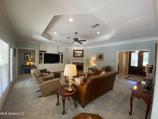 living area with ornamental molding, visible vents, a tray ceiling, ceiling fan, and a high end fireplace