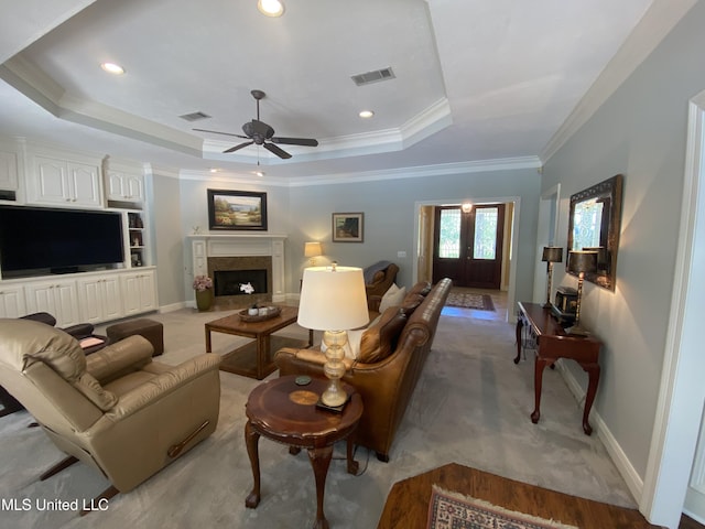 living room with a tray ceiling, ceiling fan, ornamental molding, and visible vents