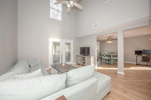 living room with a high ceiling, light hardwood / wood-style flooring, french doors, and ceiling fan