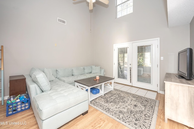 living room with ceiling fan, french doors, a towering ceiling, and light wood-type flooring