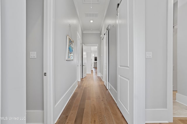 hallway featuring crown molding, a barn door, and light wood-type flooring