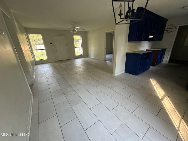 kitchen with blue cabinetry, light tile patterned floors, and ceiling fan with notable chandelier