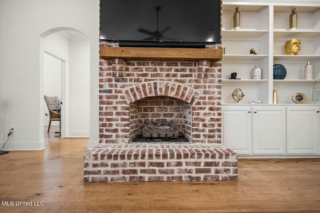 interior details featuring arched walkways, a fireplace, wood finished floors, and baseboards