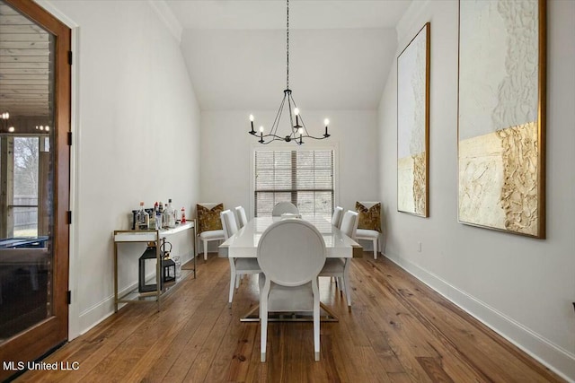 dining room featuring baseboards, hardwood / wood-style floors, vaulted ceiling, and a notable chandelier