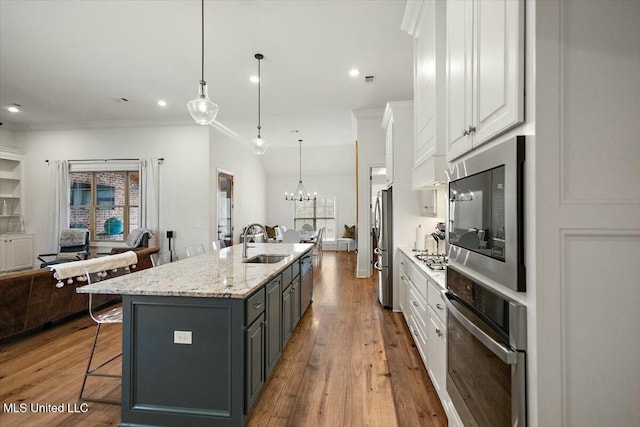 kitchen with a breakfast bar, stainless steel appliances, open floor plan, white cabinets, and a sink