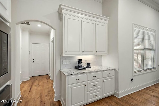 bar with arched walkways, light wood-style flooring, visible vents, baseboards, and backsplash