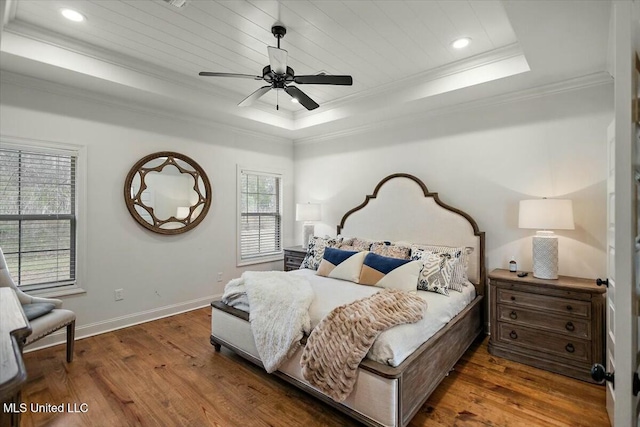 bedroom with hardwood / wood-style flooring, recessed lighting, baseboards, a raised ceiling, and crown molding