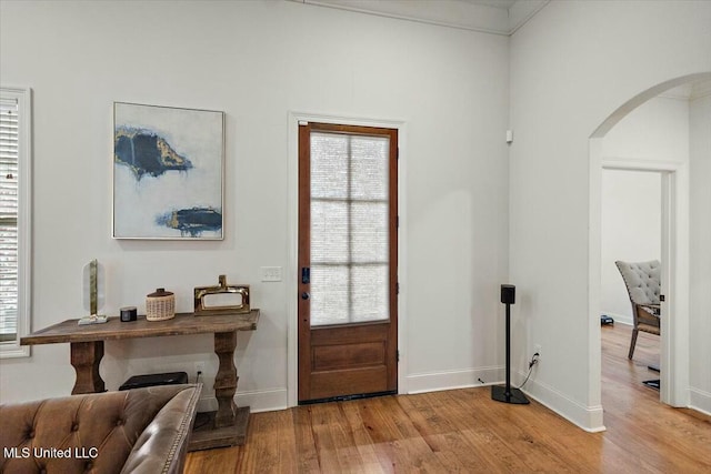 entrance foyer featuring baseboards, arched walkways, and wood finished floors