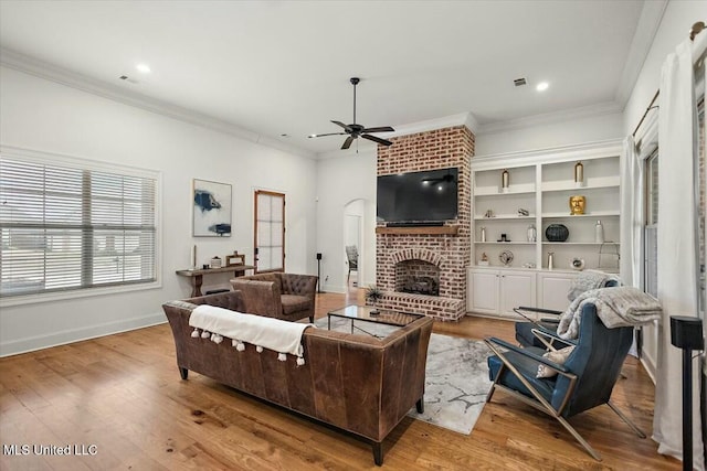 living room with a ceiling fan, a fireplace, ornamental molding, and wood finished floors