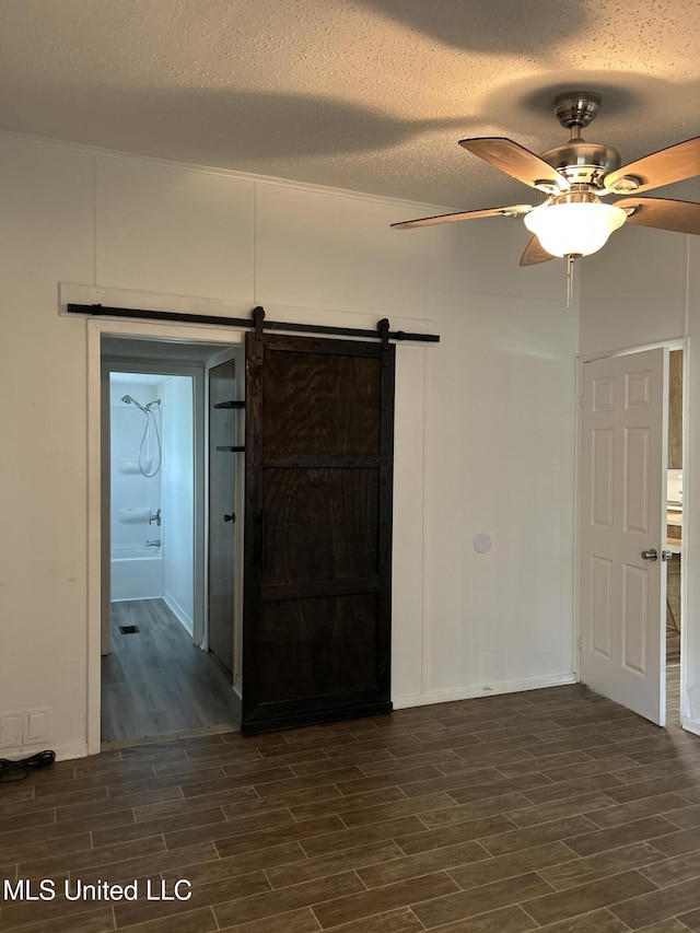 97131 Kapalama Dr, Diamondhead, MS 39525 - unfurnished room with dark wood-style flooring, a barn door, a ceiling fan, a textured ceiling, and baseboards