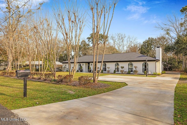 view of front of property featuring concrete driveway, a chimney, and a front yard