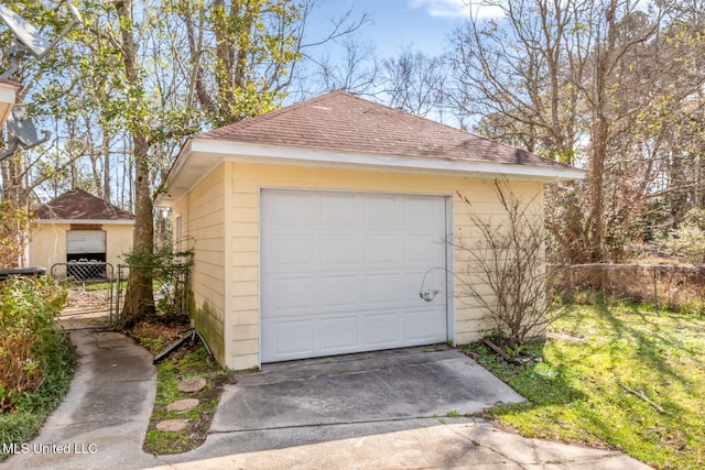 detached garage featuring concrete driveway and fence