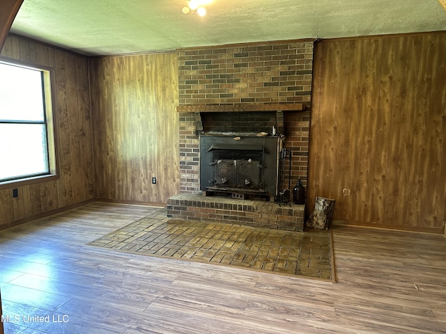 unfurnished living room with wood walls, a textured ceiling, wood finished floors, and baseboards