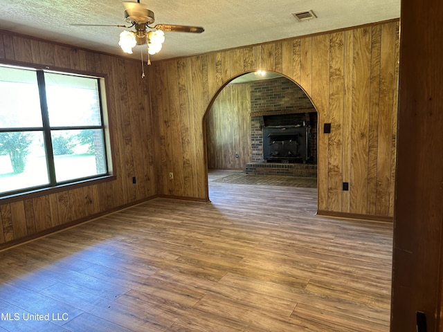 unfurnished room with a ceiling fan, visible vents, wood walls, a textured ceiling, and hardwood / wood-style flooring