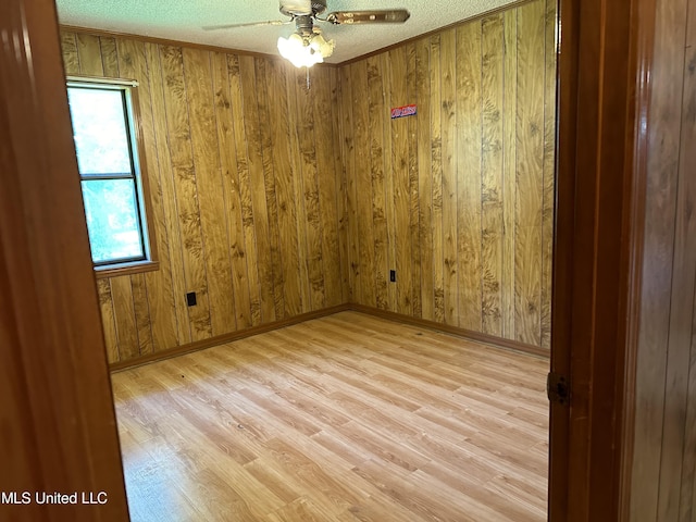 empty room featuring wood walls, a ceiling fan, and light wood finished floors