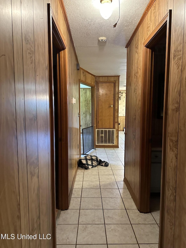 hallway featuring light tile patterned floors, a textured ceiling, visible vents, wooden walls, and crown molding