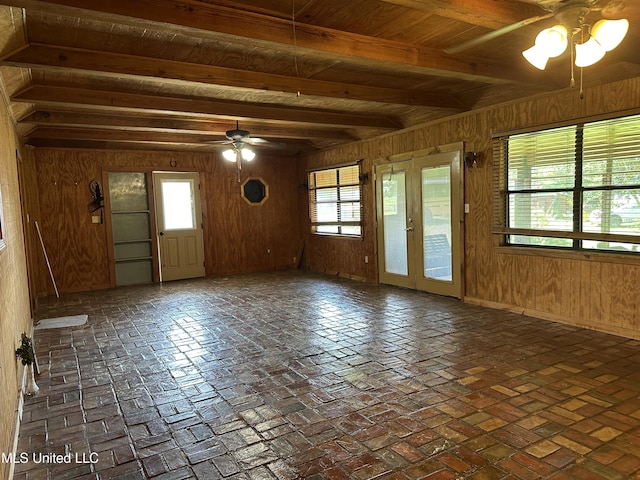 unfurnished room with beamed ceiling, ceiling fan, wooden walls, and brick floor