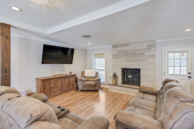 living room featuring crown molding, a large fireplace, a textured ceiling, and light wood-type flooring