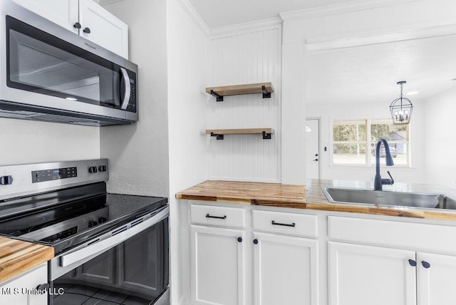 kitchen with appliances with stainless steel finishes, sink, white cabinets, and decorative light fixtures