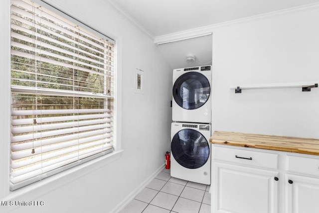 clothes washing area featuring light tile patterned flooring, ornamental molding, and stacked washer and clothes dryer