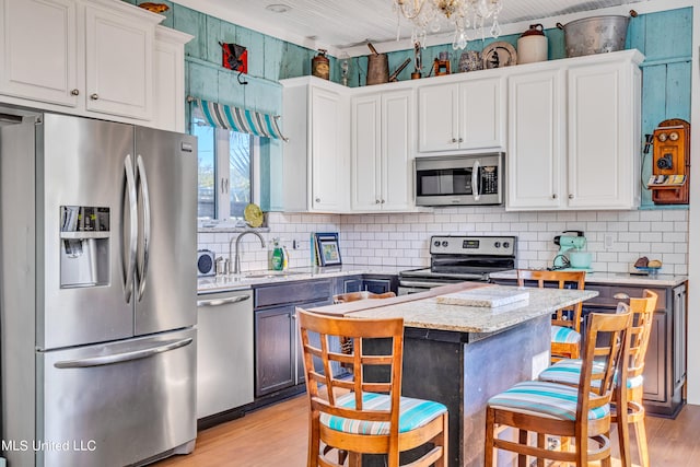 kitchen featuring light hardwood / wood-style flooring, stainless steel appliances, light stone countertops, white cabinetry, and tasteful backsplash