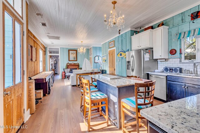 253 Sycamore St, Bay Saint Louis, MS 39520 - kitchen with white cabinets, appliances with stainless steel finishes, light stone counters, light wood-style floors, and a chandelier