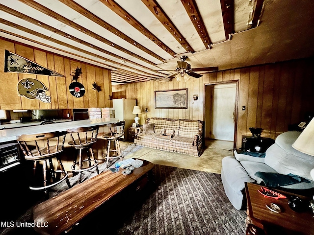 living room with wooden walls, beam ceiling, and ceiling fan