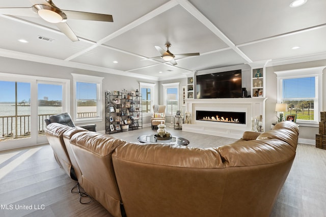 living room featuring ceiling fan, coffered ceiling, light hardwood / wood-style floors, a water view, and crown molding