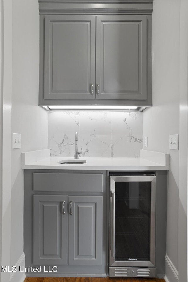 bar featuring beverage cooler, backsplash, a sink, and wet bar