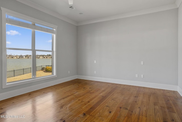 empty room with hardwood / wood-style flooring, baseboards, visible vents, and ornamental molding