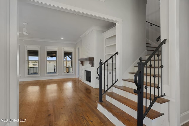 stairs featuring recessed lighting, a fireplace, wood finished floors, baseboards, and ornamental molding