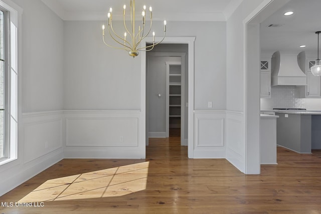 unfurnished dining area with an inviting chandelier, wood finished floors, visible vents, and crown molding