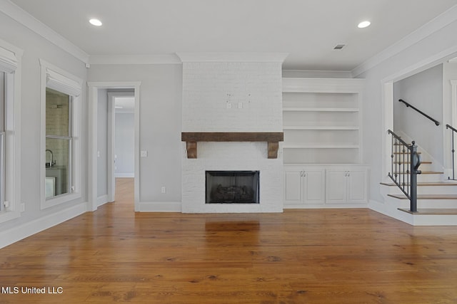 unfurnished living room featuring stairs, a fireplace, wood finished floors, and crown molding