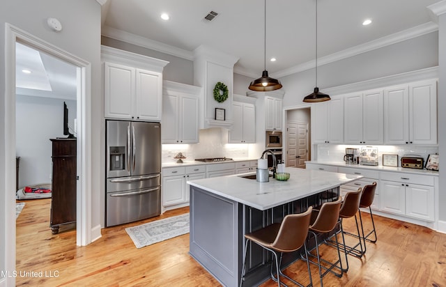 kitchen featuring a breakfast bar area, appliances with stainless steel finishes, a kitchen island with sink, light stone countertops, and white cabinets