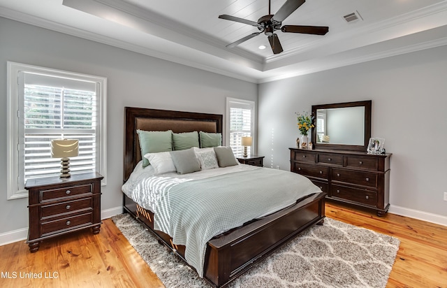 bedroom with multiple windows, light hardwood / wood-style floors, and a raised ceiling